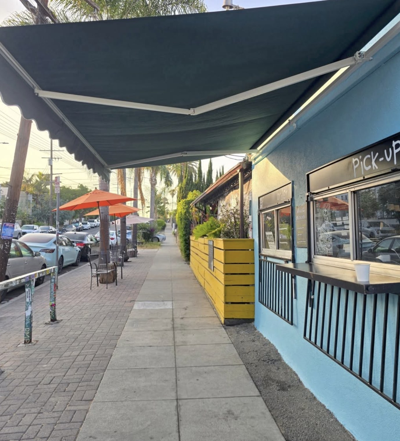 The blue storefront and pick up window at Cafecito Organico, with orange patio umbrellas outside
